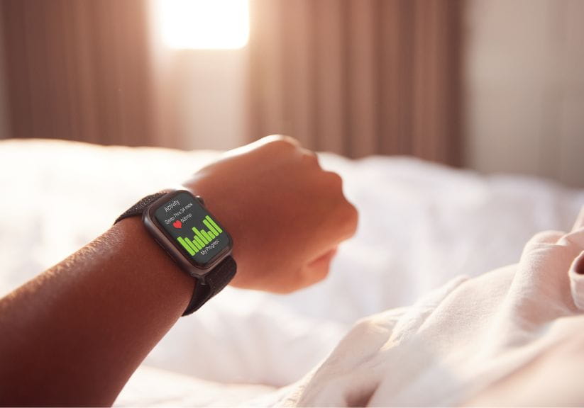 A woman looks at her smart watch while in bed to check her sleep