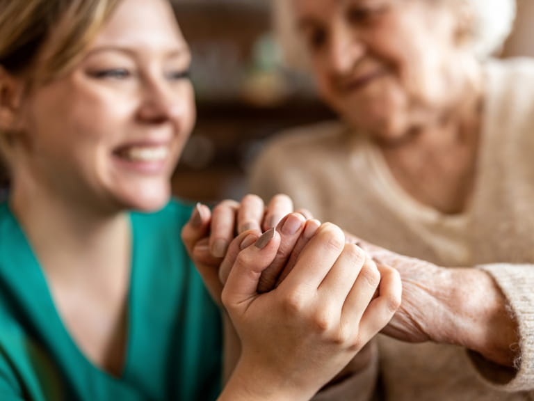An elderly woman holding hands with a smiling nurse in green scrubs