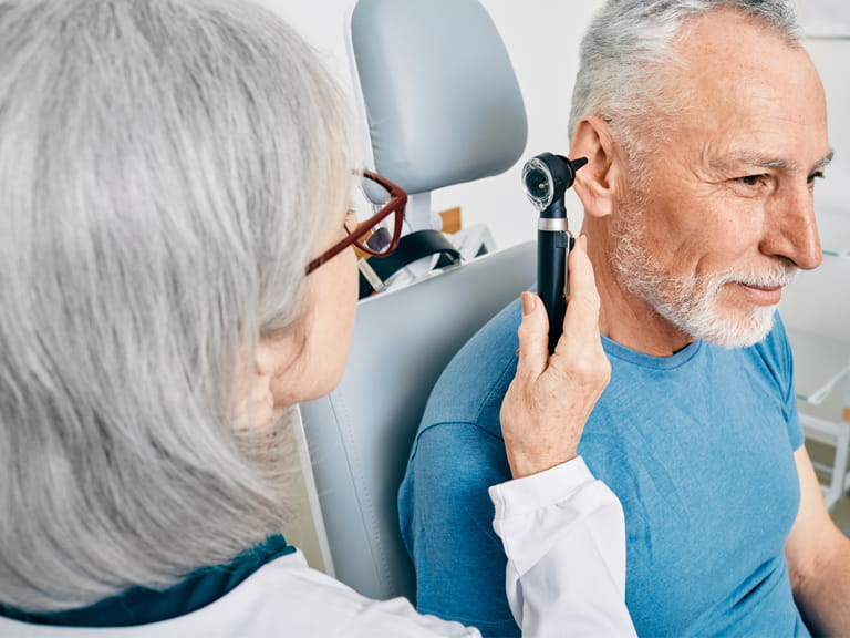 Otolaryngologist doctor checking senior man's ear using otoscope or auriscope at hearing center. Audiology