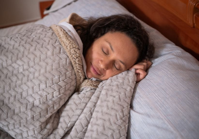 A woman sleeps under a weighted blanket