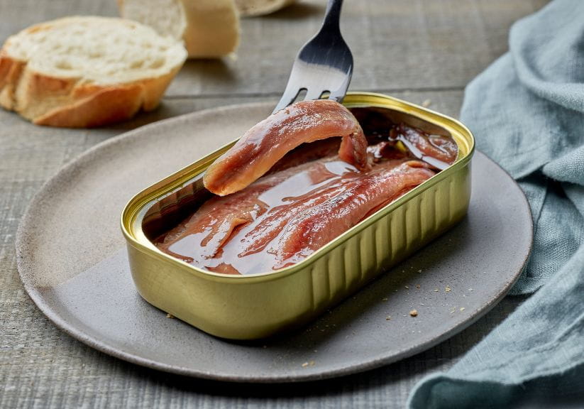 Someone putting a fork into a tin of anchovy fillets