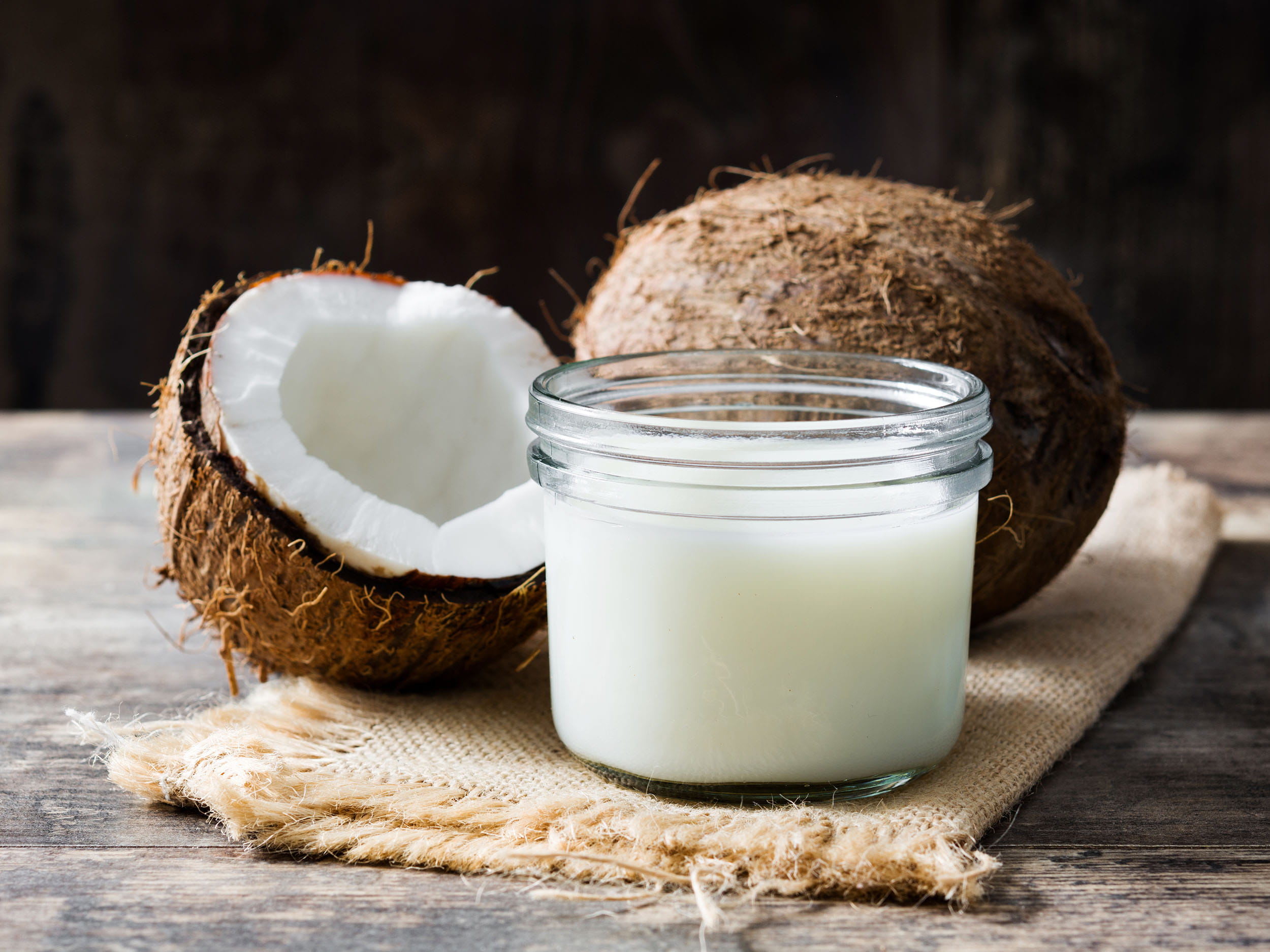 A coconut split in half next to a jar of coconut oil