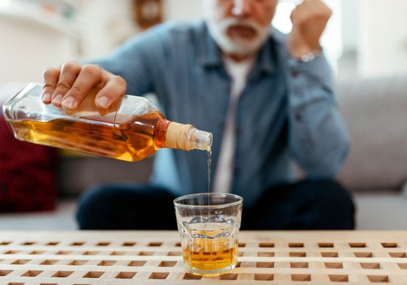 A man pours a whiskey into a tumbler on a table in front of him