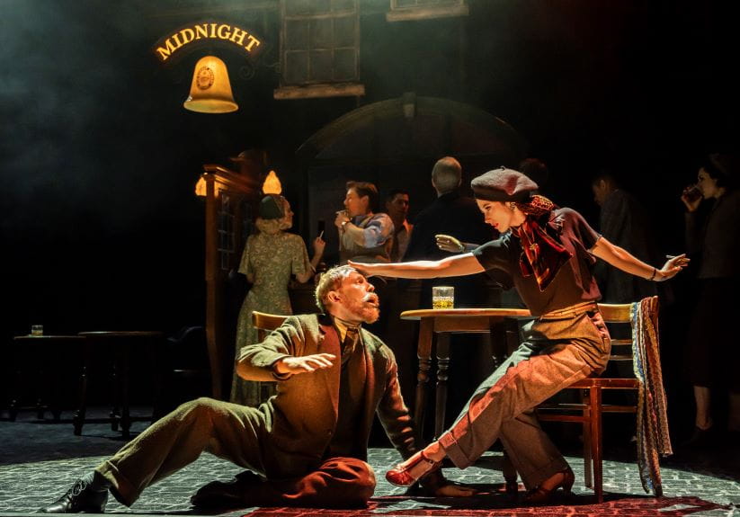 Woman and man sitting outside a pub on stage, with her holding his head up and away