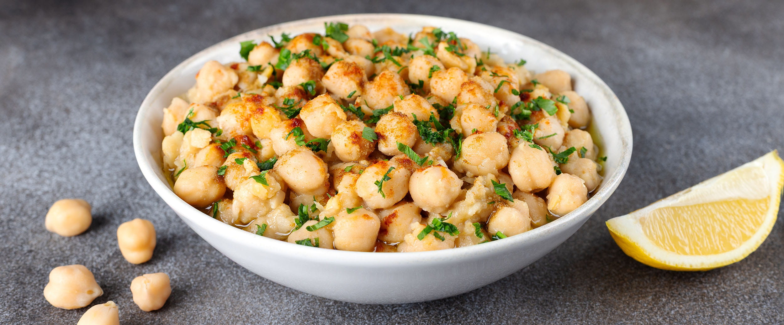 A bowl of cooked chickpeas with a wedge of lemon