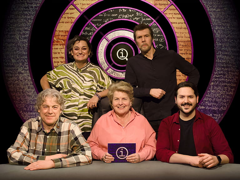 The QI crew on set behind the desk