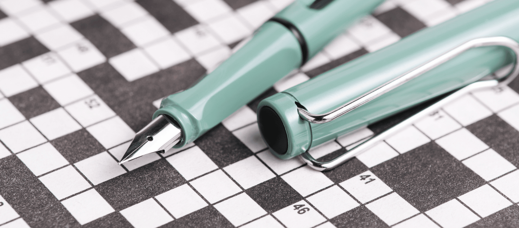 A crossword puzzle with an emerald green fountain pen lying over it