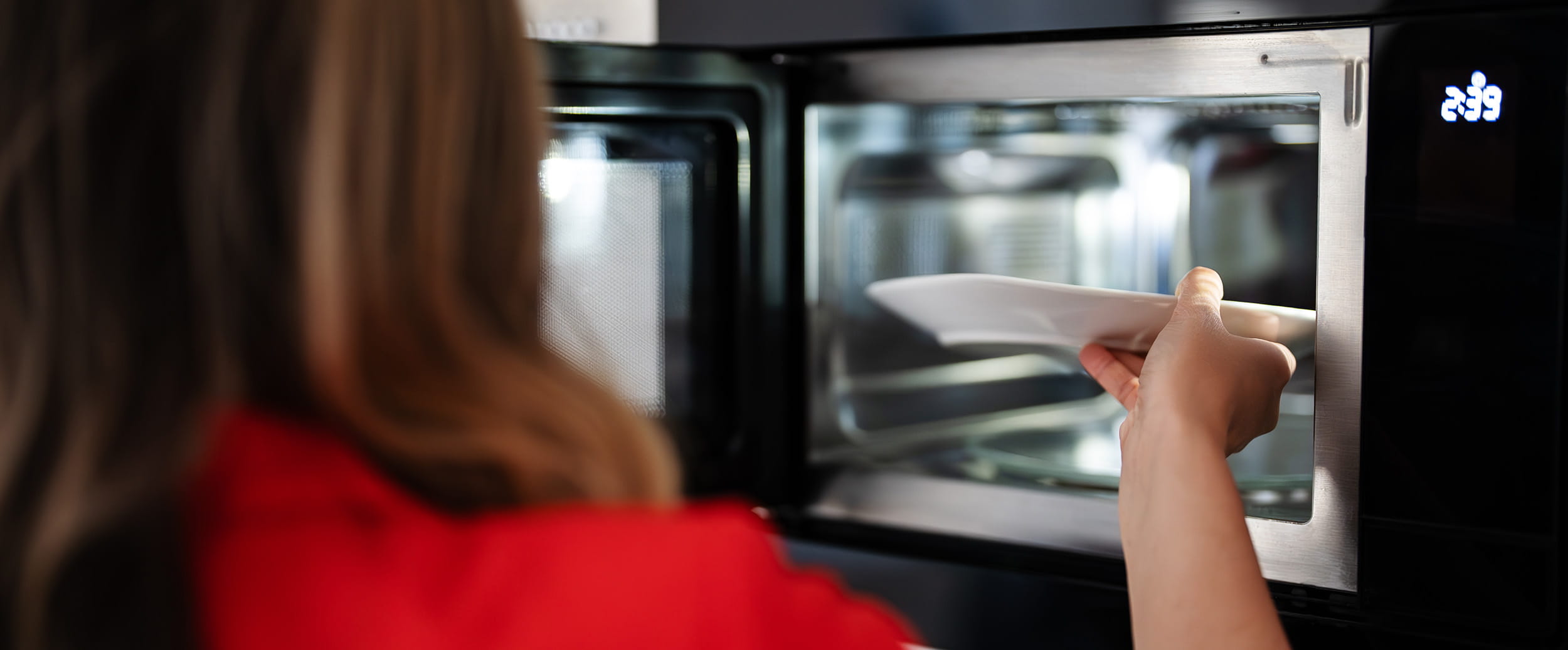 A woman puts a plate into the microwave