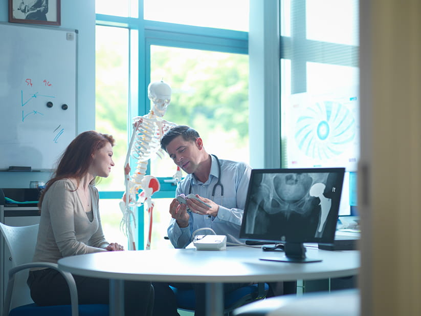 A doctor demonstrating a hip joint next to an x-ray of a replaced hip joint