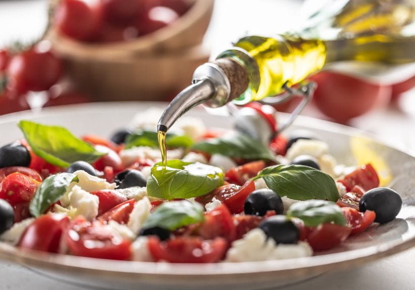 A close up of a greek salad with olive oil being poured over it