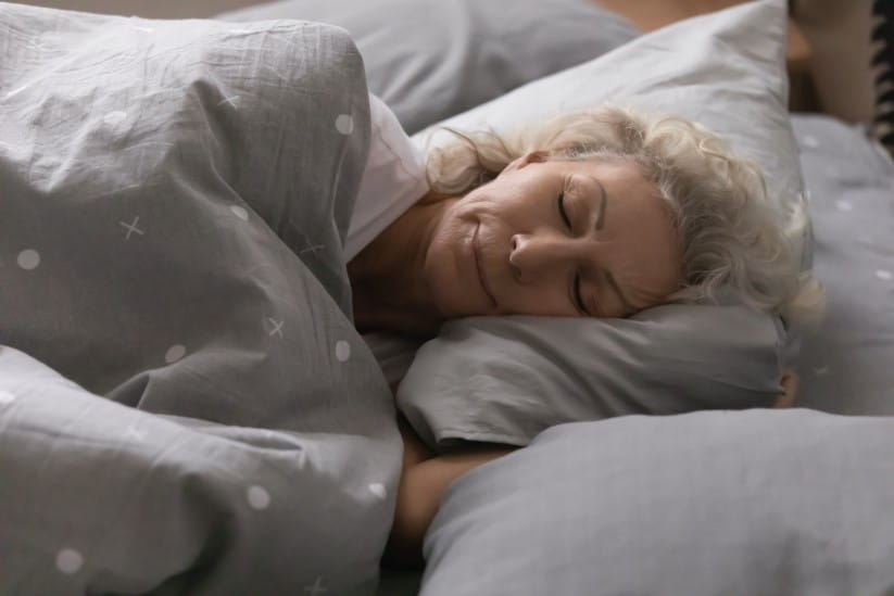 An older woman sleeping in her bed happily