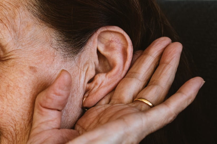 An older woman with her hand up to her ear, trying to hear