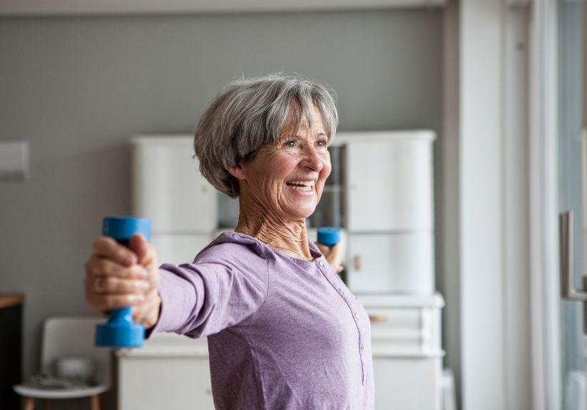 An older lady lifts dumbbells at home