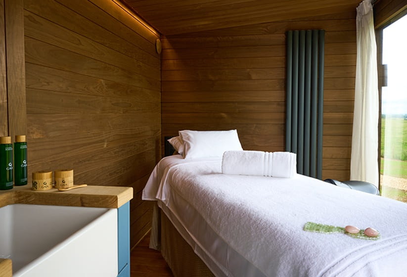 Spa treatment bed with white towels inside wooden cabin