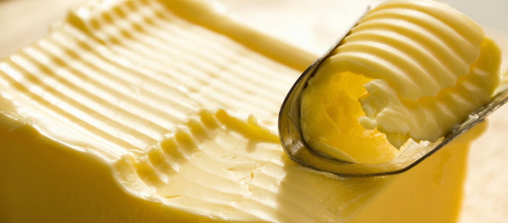 A knife scraping a curl of butter off a pack