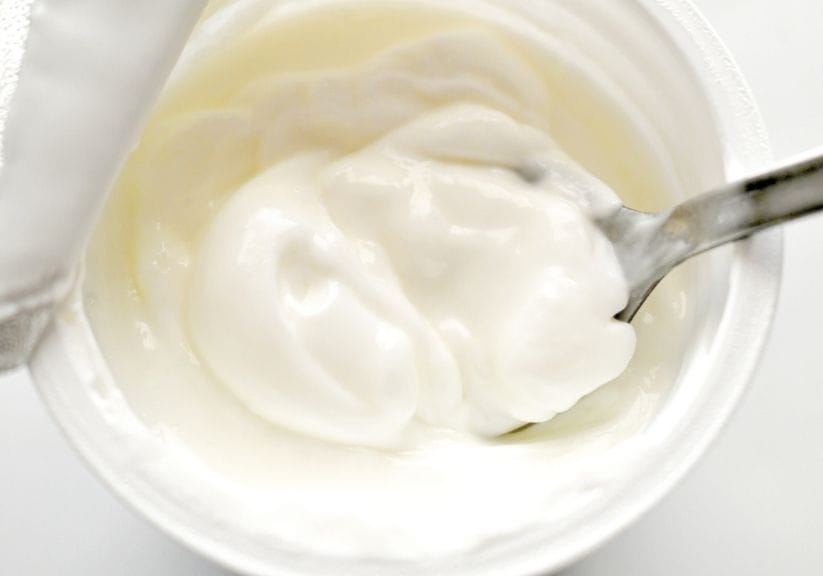 An open tub of natural yoghurt with a spoon in it