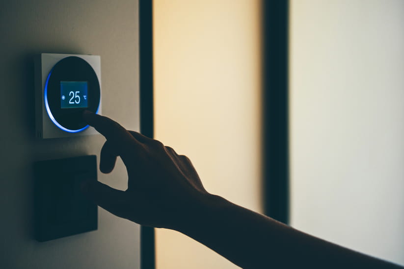 A silhouetted hand is seen adjusting an electric thermostat on the wall