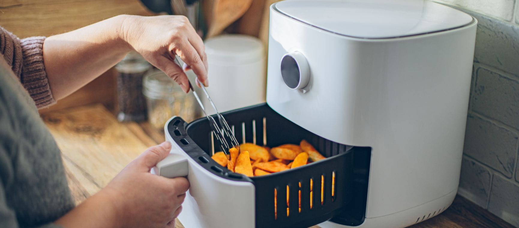 A person cooking potatoes in an air fryer with the drawer half way open