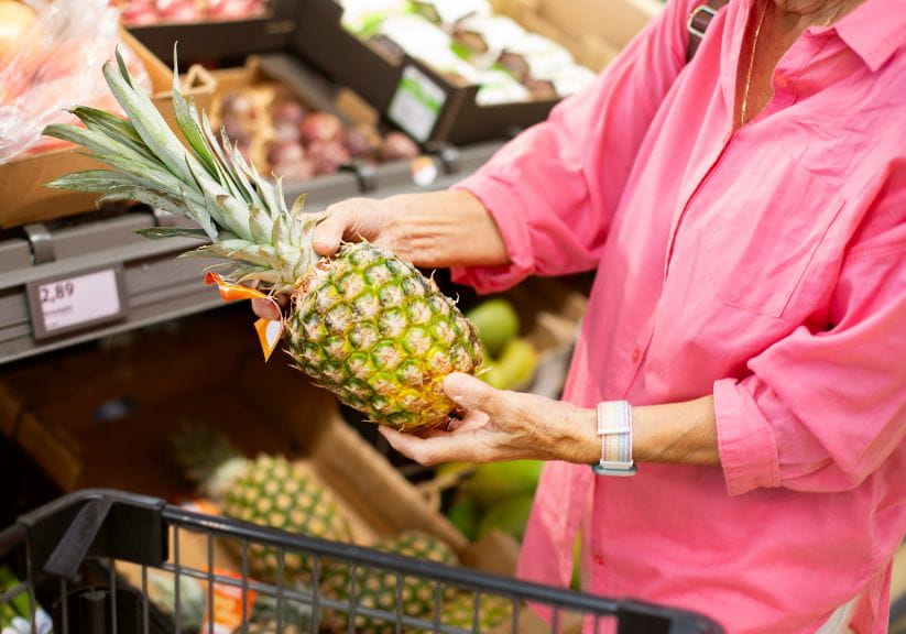 A woman in a pink shirt picking up a pineapple at a supermarket