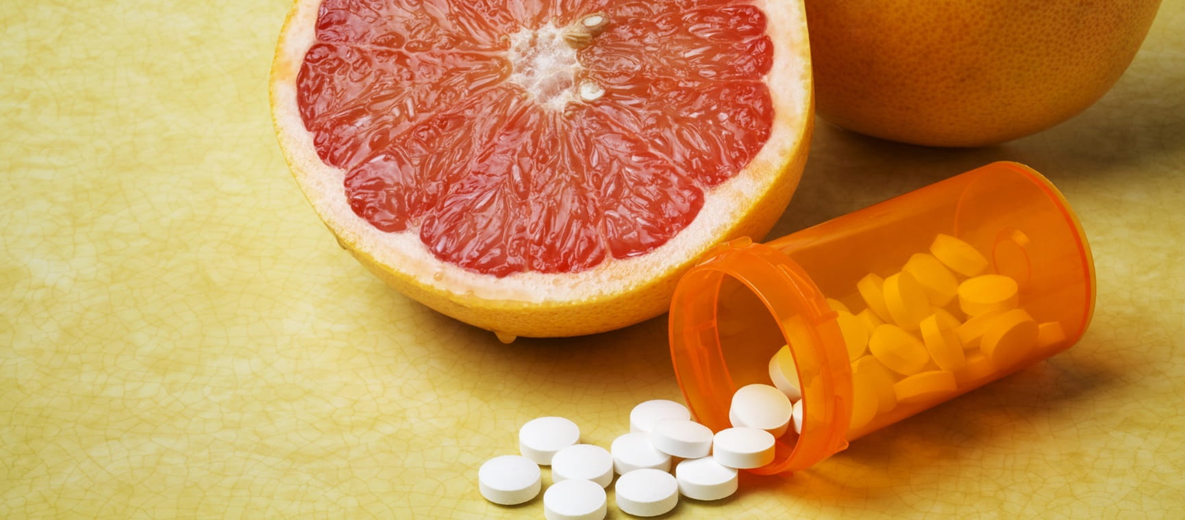 A cut grapefruit beside an open bottle of tablets spilled onto the surface