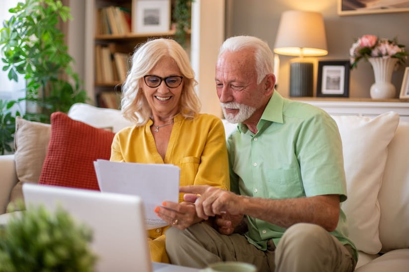 An older man and woman sat on the sofa looking at papers