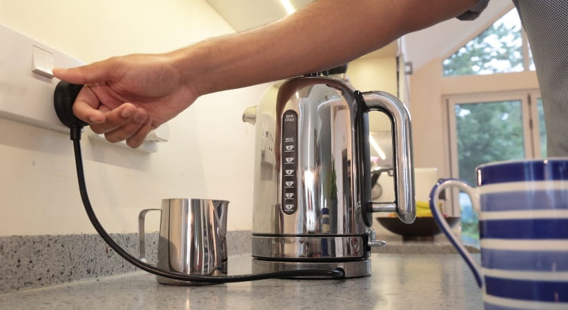 Person switching a kettle on at the wall
