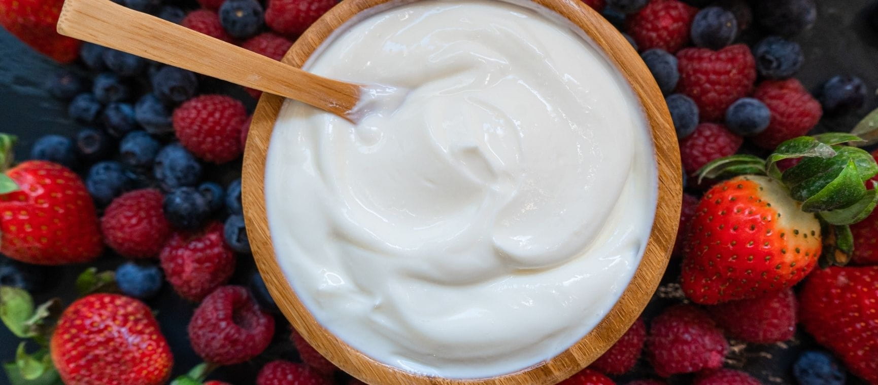 A wooden bowl full of yoghurt on a background of red fruit