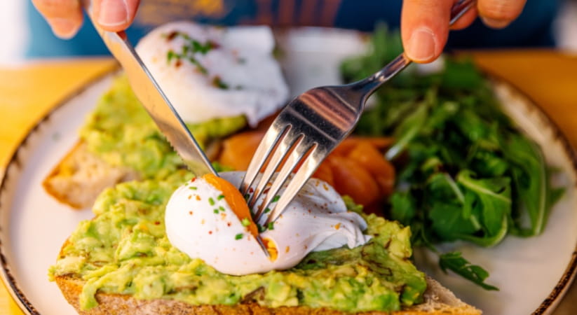 A person eating poached eggs and avocado on toast