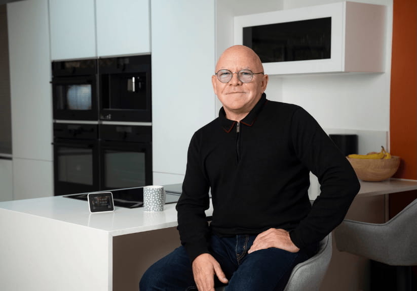 TV presenter Dominic Littlewood sitting at a breakfast bar in a kitchen
