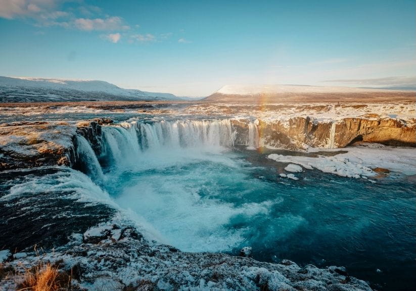 aerial view of Godafoss Falls near mountains against sky at sunset during winter