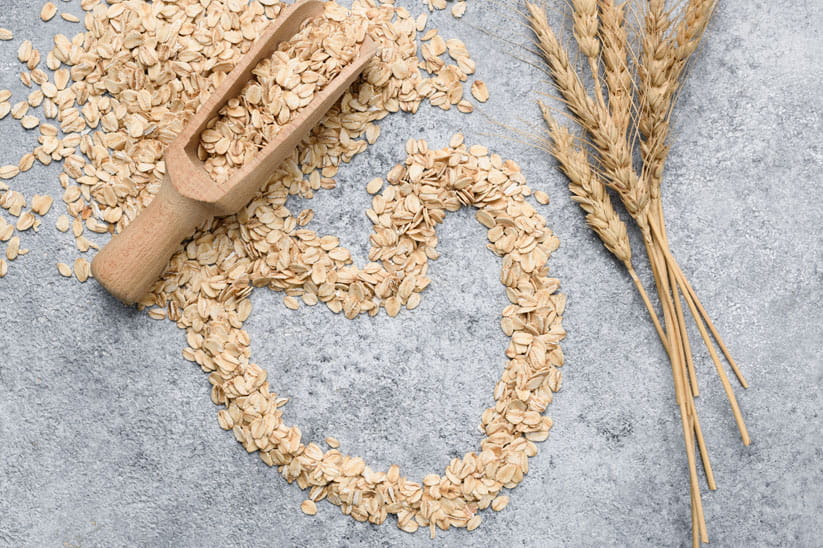 Oats arranged in a heart-shape with stalks of oats and a spoon overflowing with oats next to it