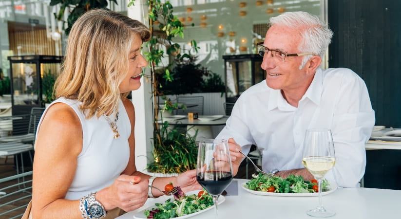 Older couple in white looking at each other as they eat a salad in a restaurant