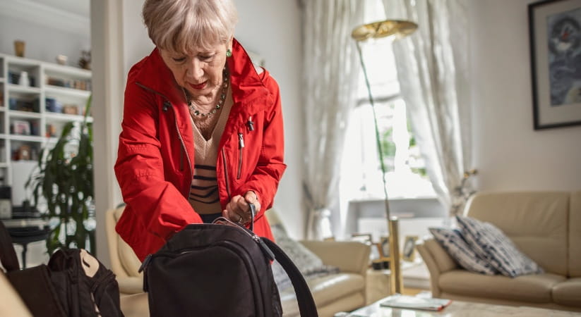 Older woman in red coat loading rucksack in house