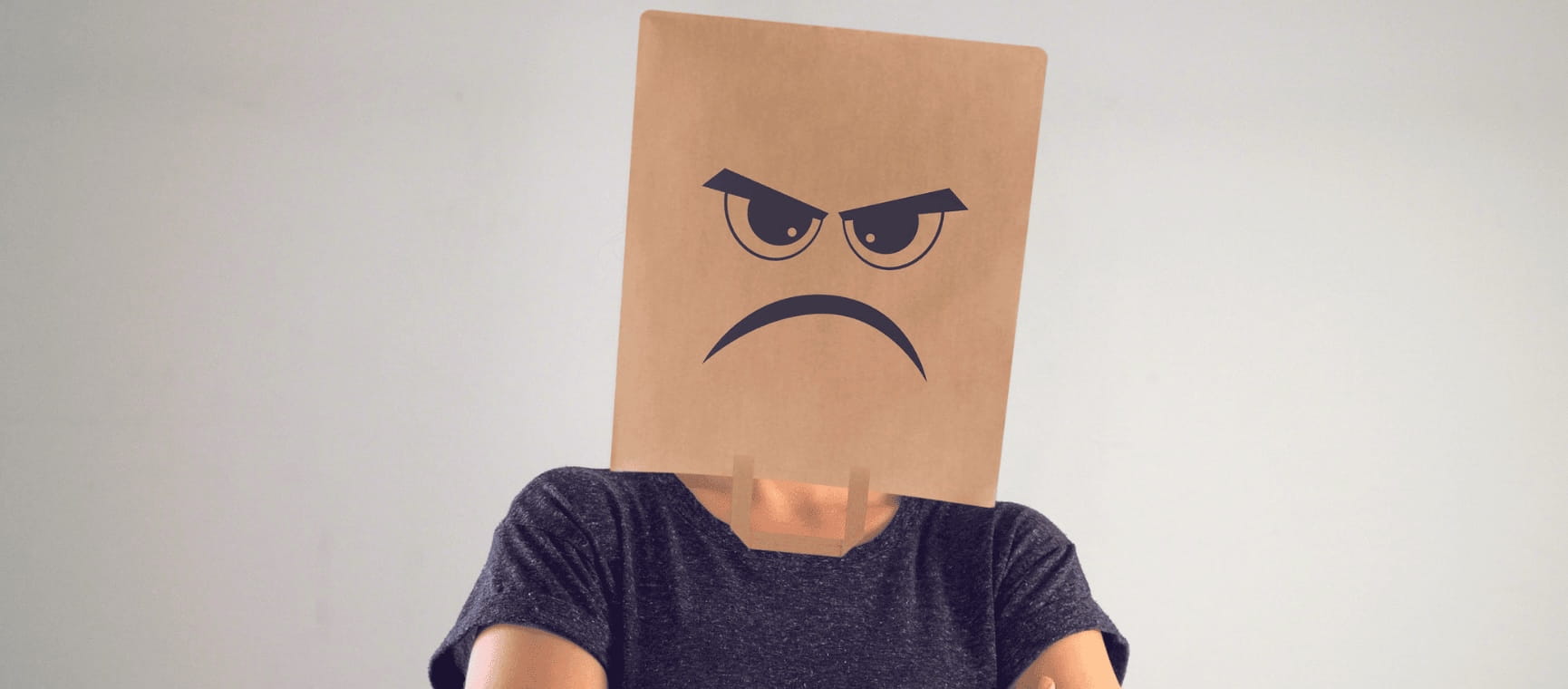 A woman wearing a bag over her head with a grumpy face painted on it