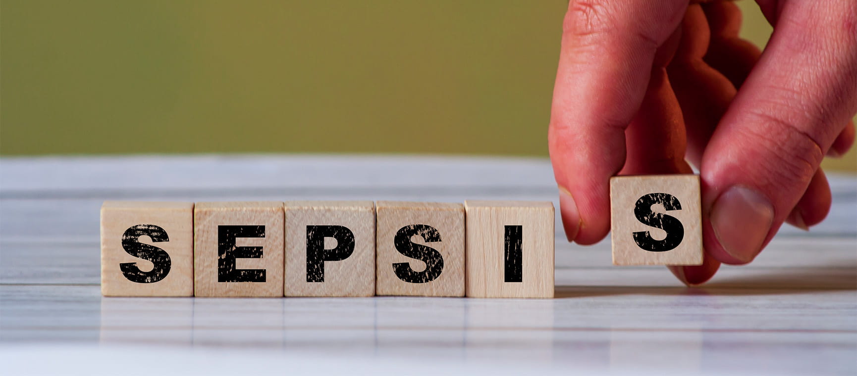 Wooden blocks with letters printed on them being placed in a row to spell sepsis