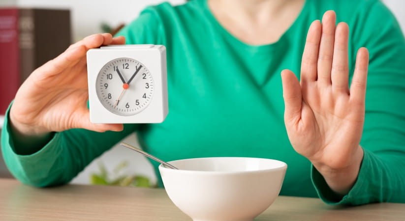 Woman in green top with an empty bowl and clock holding her hand up in a stop sign