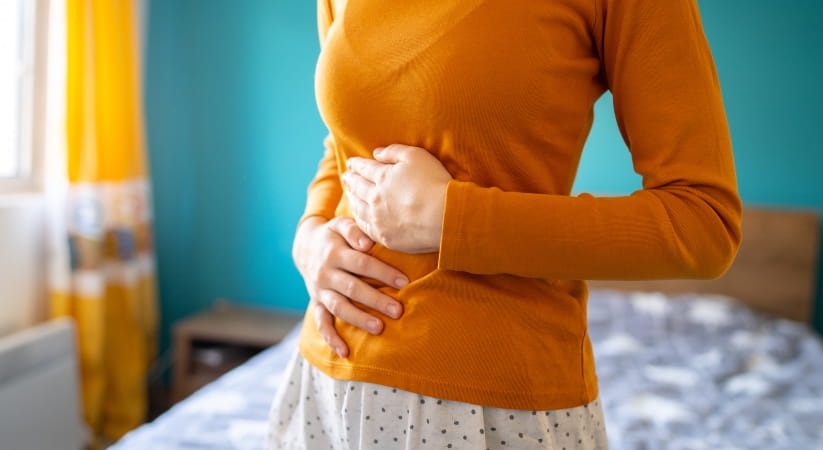 Woman in orange jumper holding her stomach with both hands
