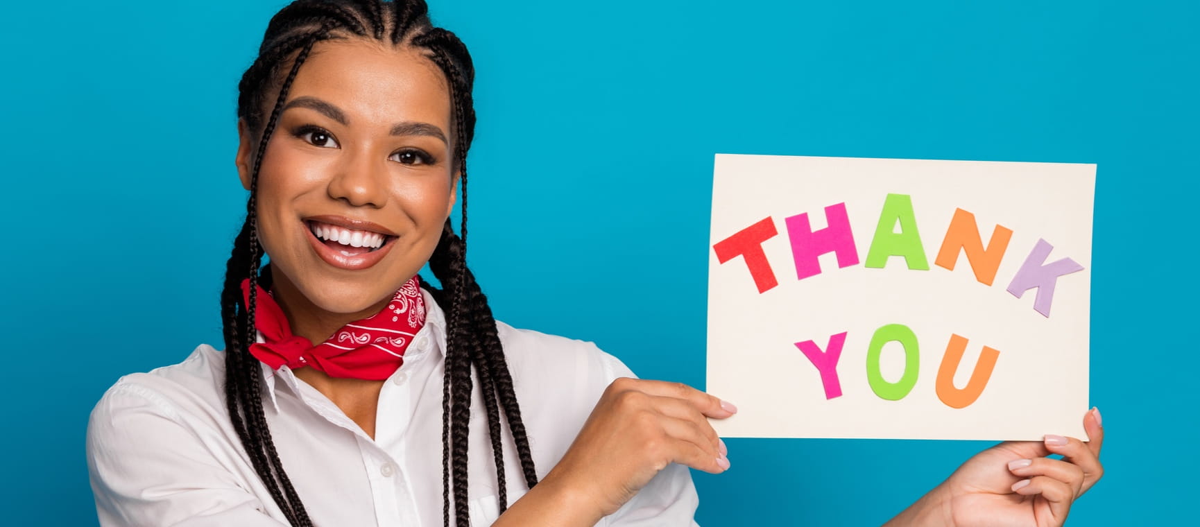 Woman smiling and holding up a sign saying thank you against a blue background
