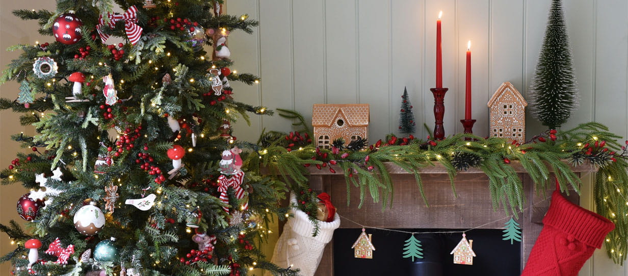 A decorated Christmas tree next to a fireplace with red candles, greenery and berries