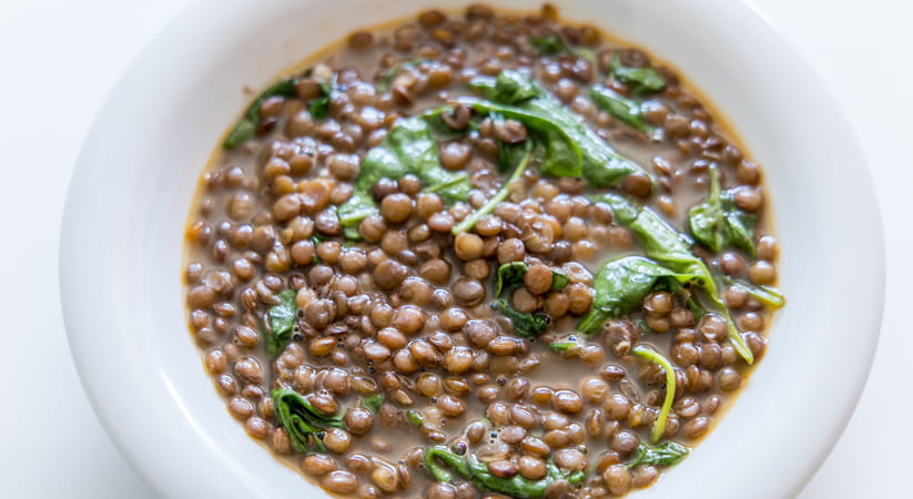 Close up of a white bowl containing lentils and spinach