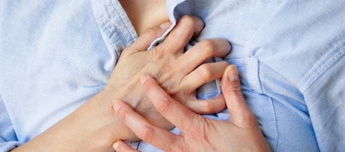 Close up of woman in a blue shirt holding her chest with both hands