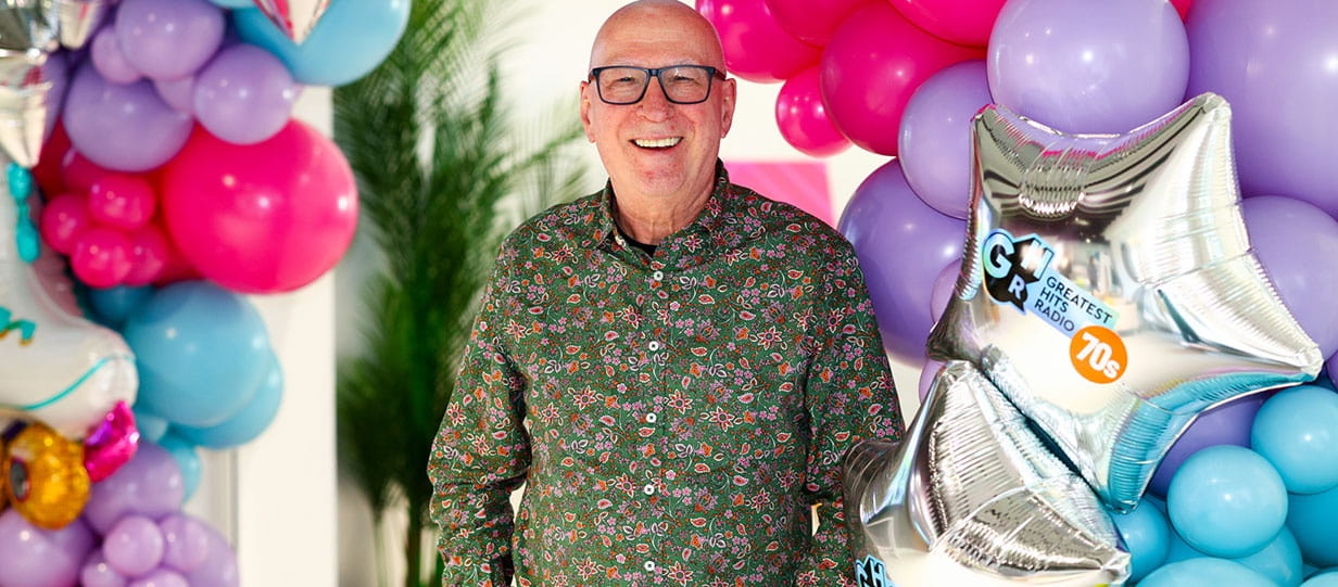 Ken Bruce of Greatest Hits Radio smiling and surrounded by balloons