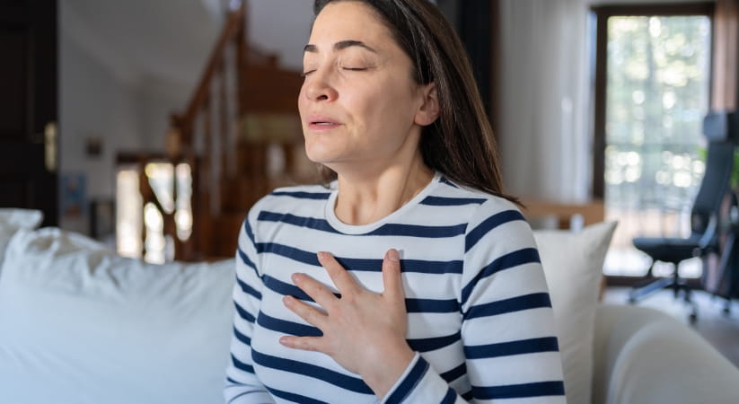 Middle aged woman in blue and white hooped top holding her chest
