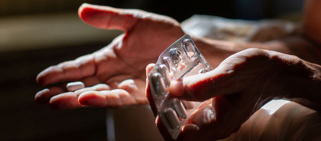 Close up of hands, a pill in one and a silver pill blister pack in the other