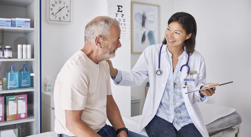 Female doctor smiling and putting her hand on a bearded mans shoulder