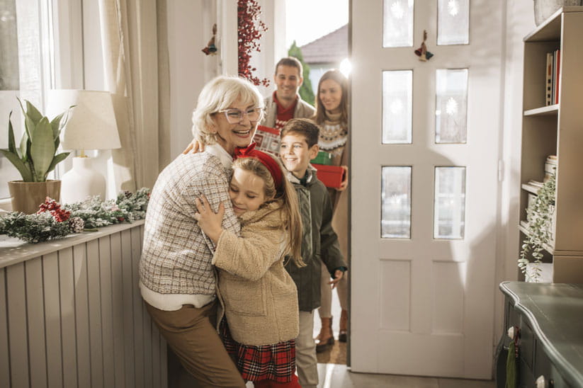An older woman greeting kids and grandkids at the door for Christmas