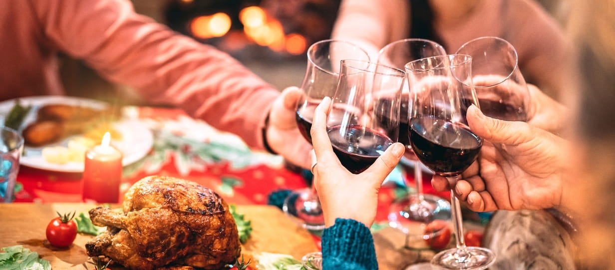 People clinking red wine glasses over Christmas dinner