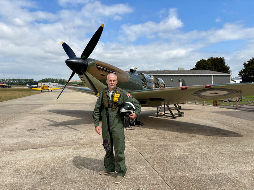 Jeremy Taylor posing in flight suit in front of a Spitfire