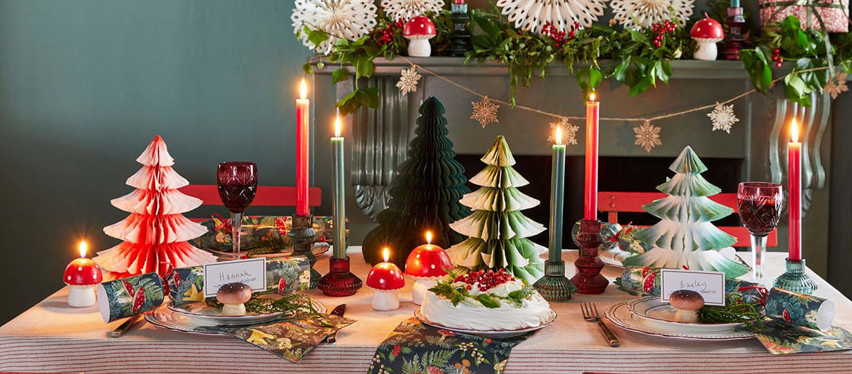 A dining table dressed for Christmas with paper tree decorations, candles and Christmas crackers