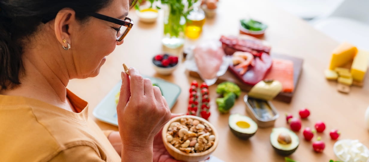 Woman holding a bowl of nuts and looking at healthy food on table
